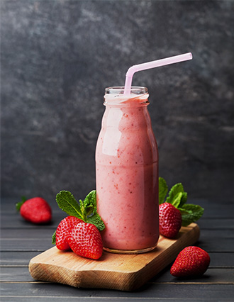 Fresh strawberry milkshake in a glass bottle with a pink straw, surrounded by strawberries and mint.