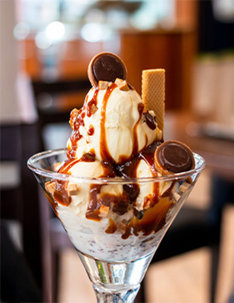 Vanilla ice cream sundae topped with caramel sauce, chocolate pieces, and a wafer stick in a glass dish.